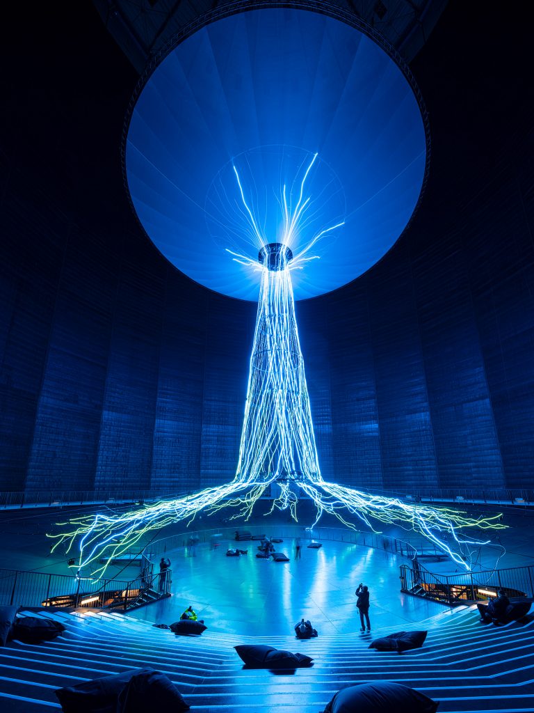 Eine abstrakte Baumskulptur aus LED-Licht im Inneren eines riesigen Gasometers, das Bild ist fast komplett Blau durch die Lichtfarbe